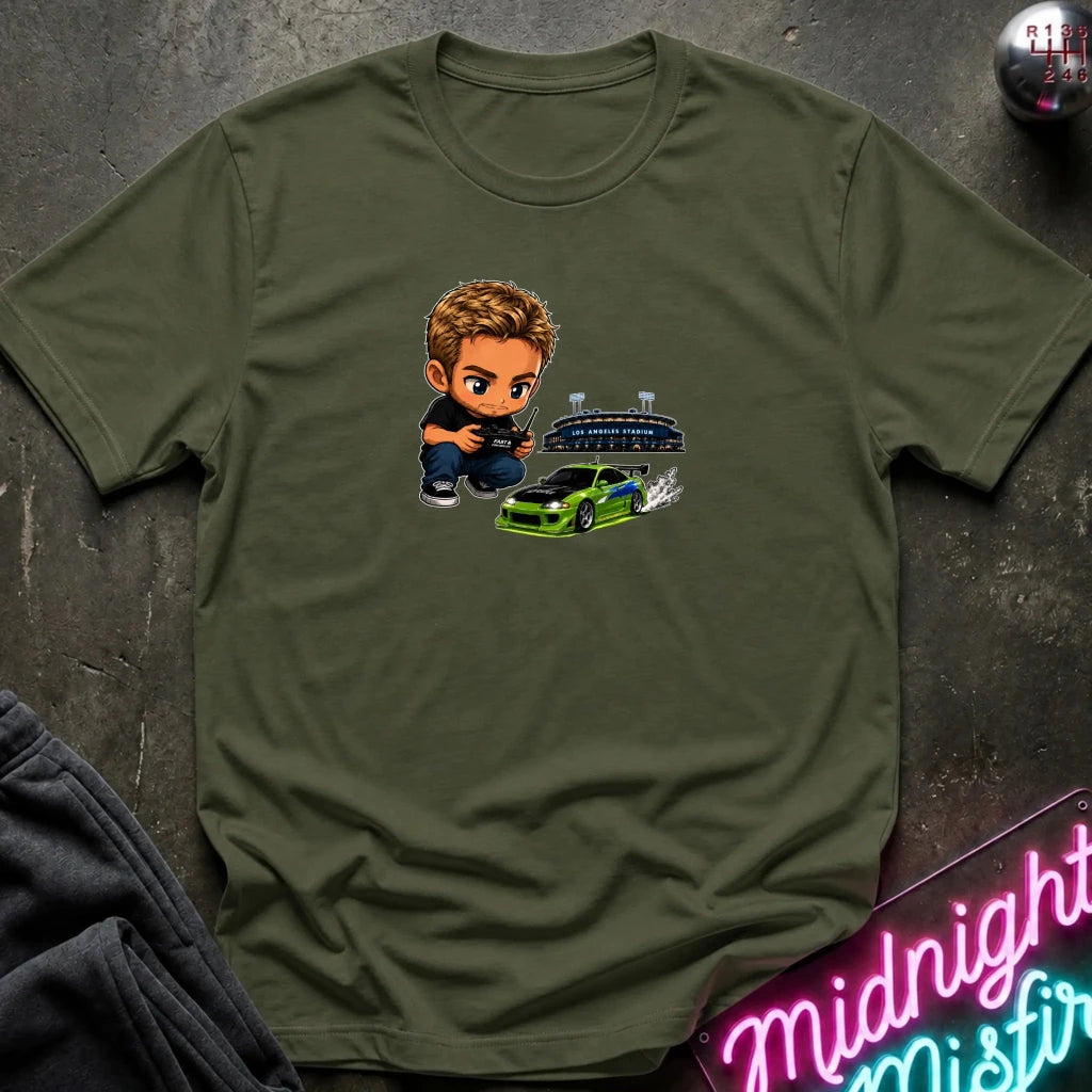 A  olive green graphic t-shirt laid flat on a dark textured surface. The graphic features a green car, and person  controlling it with remote.