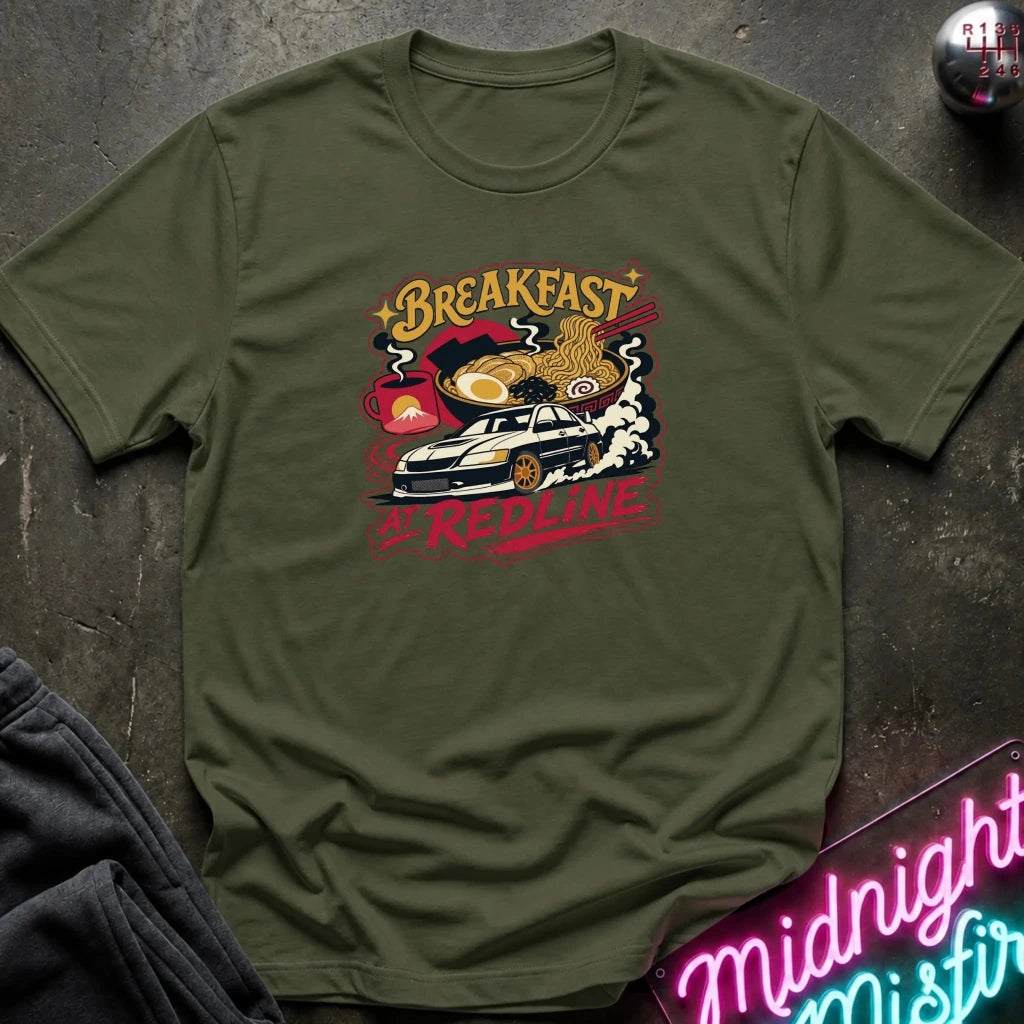 short-sleeve graphic T-shirt laid flat on a dark textured surface. The shirt features a colorful retro-style chest print with the words 'Breakfast at Redline'