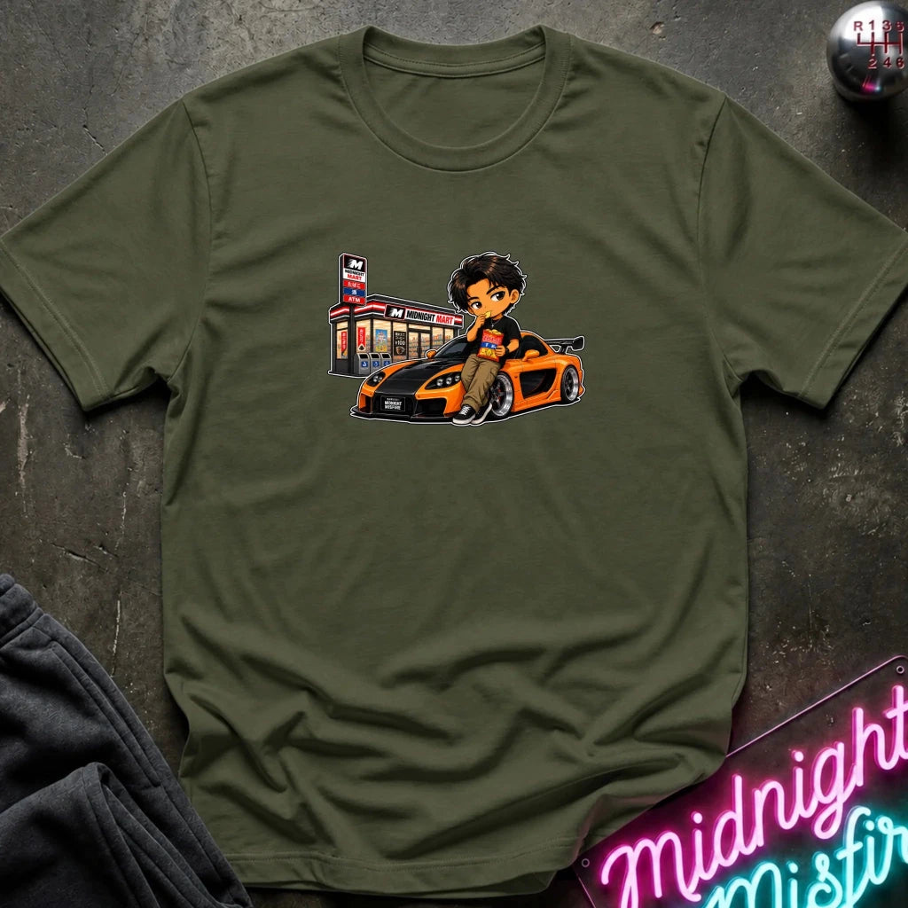 An olive green short-sleeve crewneck t-shirt laid flat on a dark textured surface, featuring a cartoon graphic of a man sitting on a orange and black sports car next to a store.