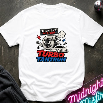 A white short-sleeve graphic T-shirt laid flat on a dark textured surface. The shirt features a colorful front print with a turbocharger, smoke, lightning bolts, a small car, and the text 'MIDNIGHT MISFIRE' and 'TURBO TANTRUM.