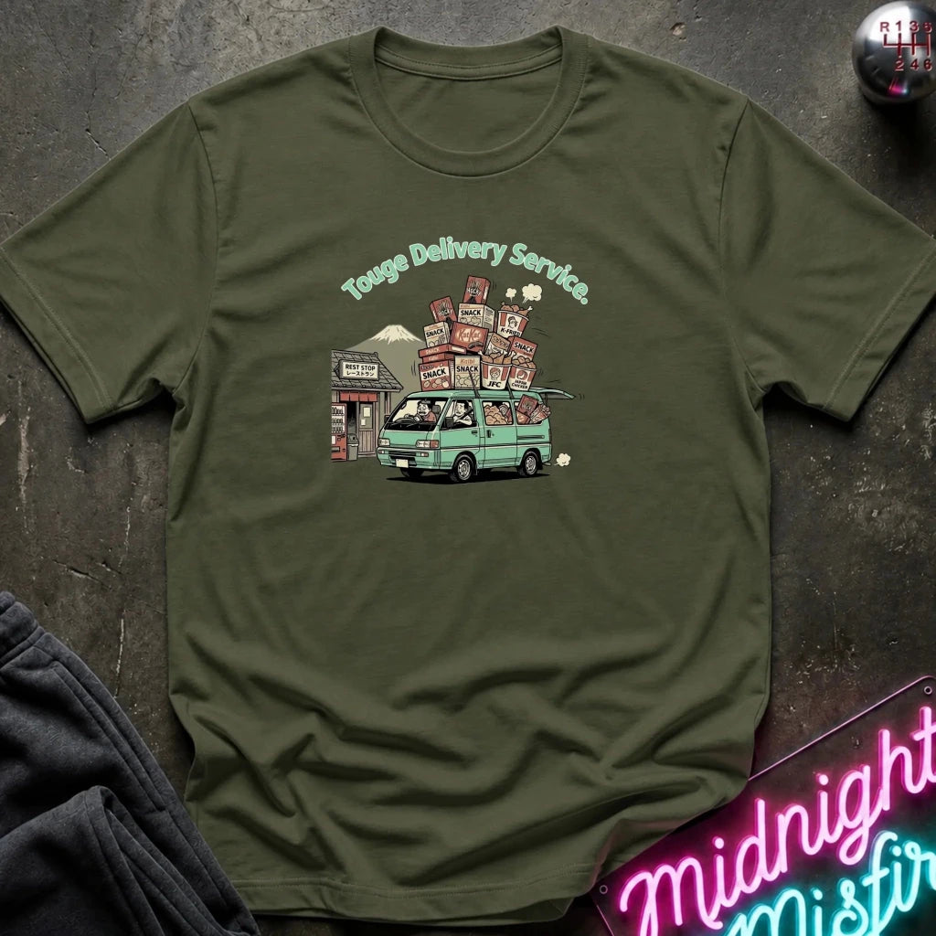 An olive green crewneck t-shirt laid flat on a dark textured surface, featuring a cartoon graphic of a light green van carrying stacked packages with the text 'Touge Delivery Service'.