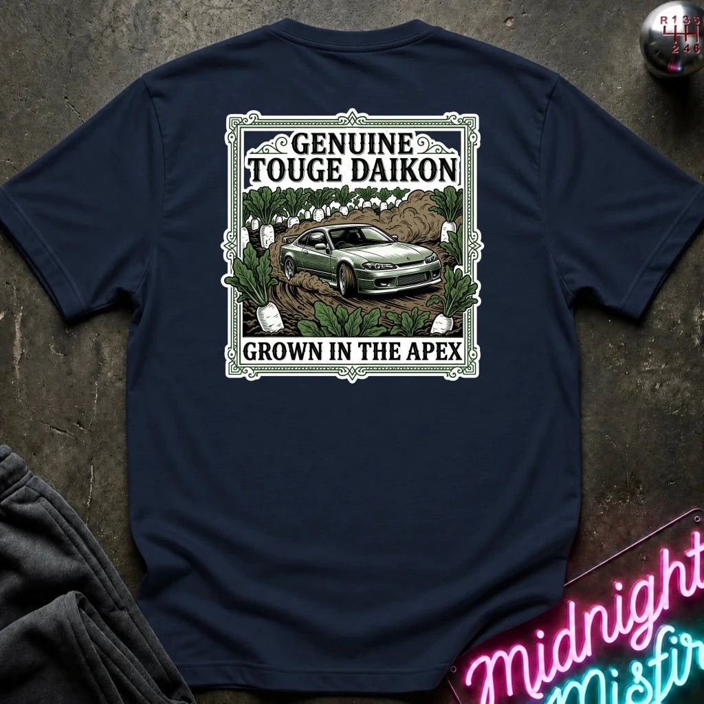 A navy blue short-sleeve graphic T-shirt laid flat on a dark textured surface. The shirt features a rectangular vintage-style print with the words 'Genuine Touge Daikon' and 'Grown in the Apex' surrounding an illustration of a green car in a field.