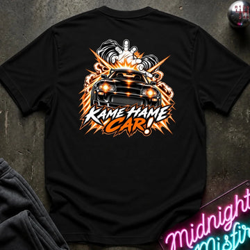 A black short-sleeve graphic T-shirt laid flat on a dark textured surface. The back of the shirt features a large orange, white, and black flame-style graphic with a car illustration and the text 'KAME HAME CAR!'.