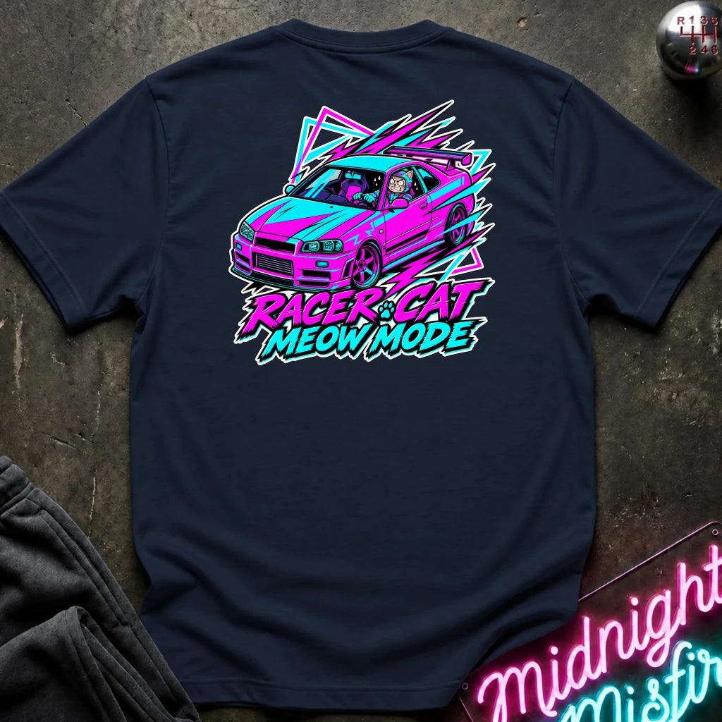 A navy blue t-shirt laid flat on a dark textured surface, featuring a colorful graphic of a pink and teal car with the text 'RACER CAT MEOW MODE' in neon pink and teal.