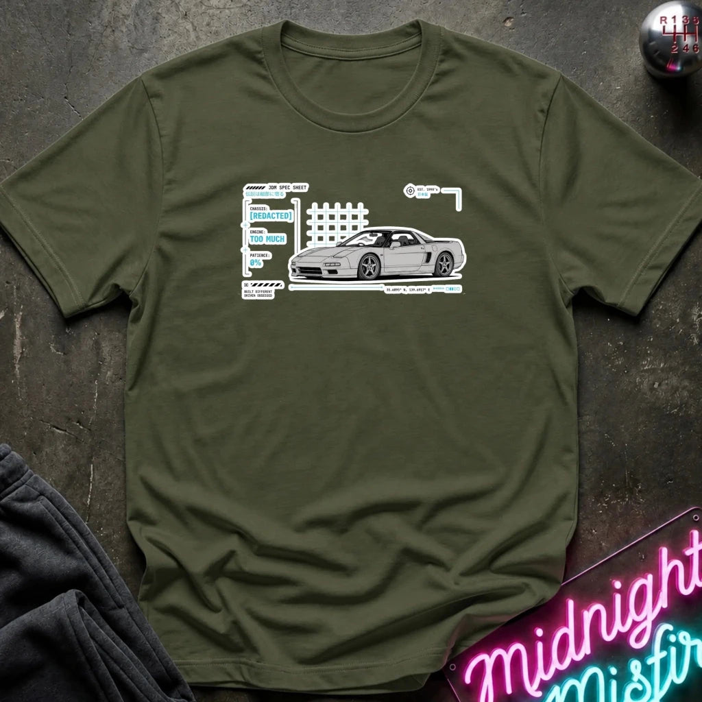 An olive green short-sleeve t-shirt with a white and gray graphic of a sports car next to a stylized track map, laid flat on a dark textured surface with a neon sign and dark pants in the background.