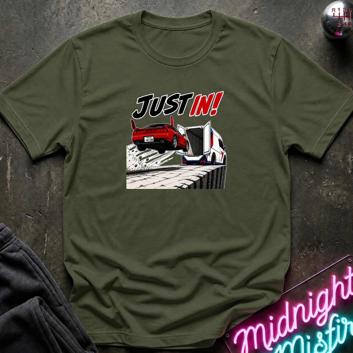 An olive green short-sleeved t-shirt  that has a red car jumping into back of another machine.