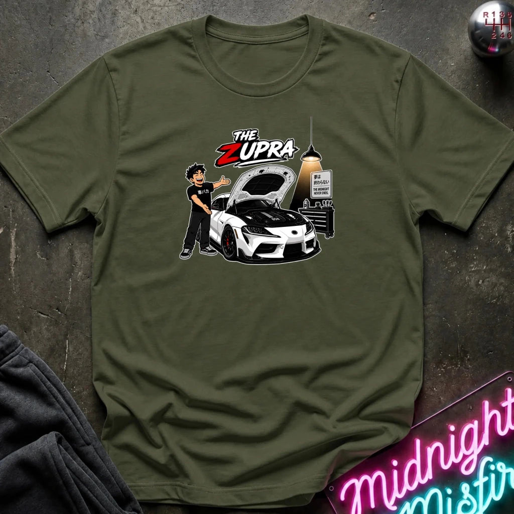 An olive green short-sleeve graphic t-shirt laid flat on a dark textured surface. The graphic features a cartoon illustration of a man standing next to a white sports car with its hood open, under the text 'THE ZUPRA'.