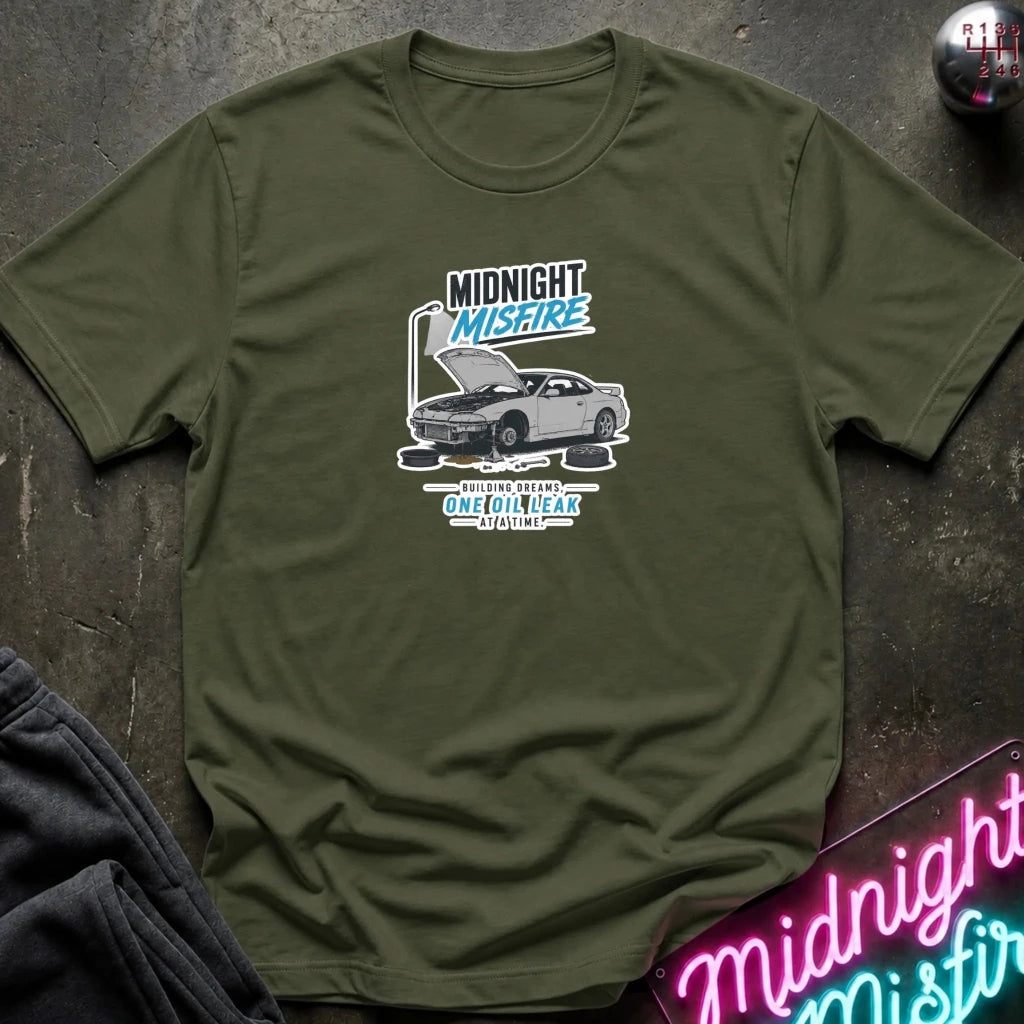 An olive green short-sleeve t-shirt with a graphic print of a silver Nissan Sentra with its hood open, featuring the text 'MIDNIGHT MISFIRE' 