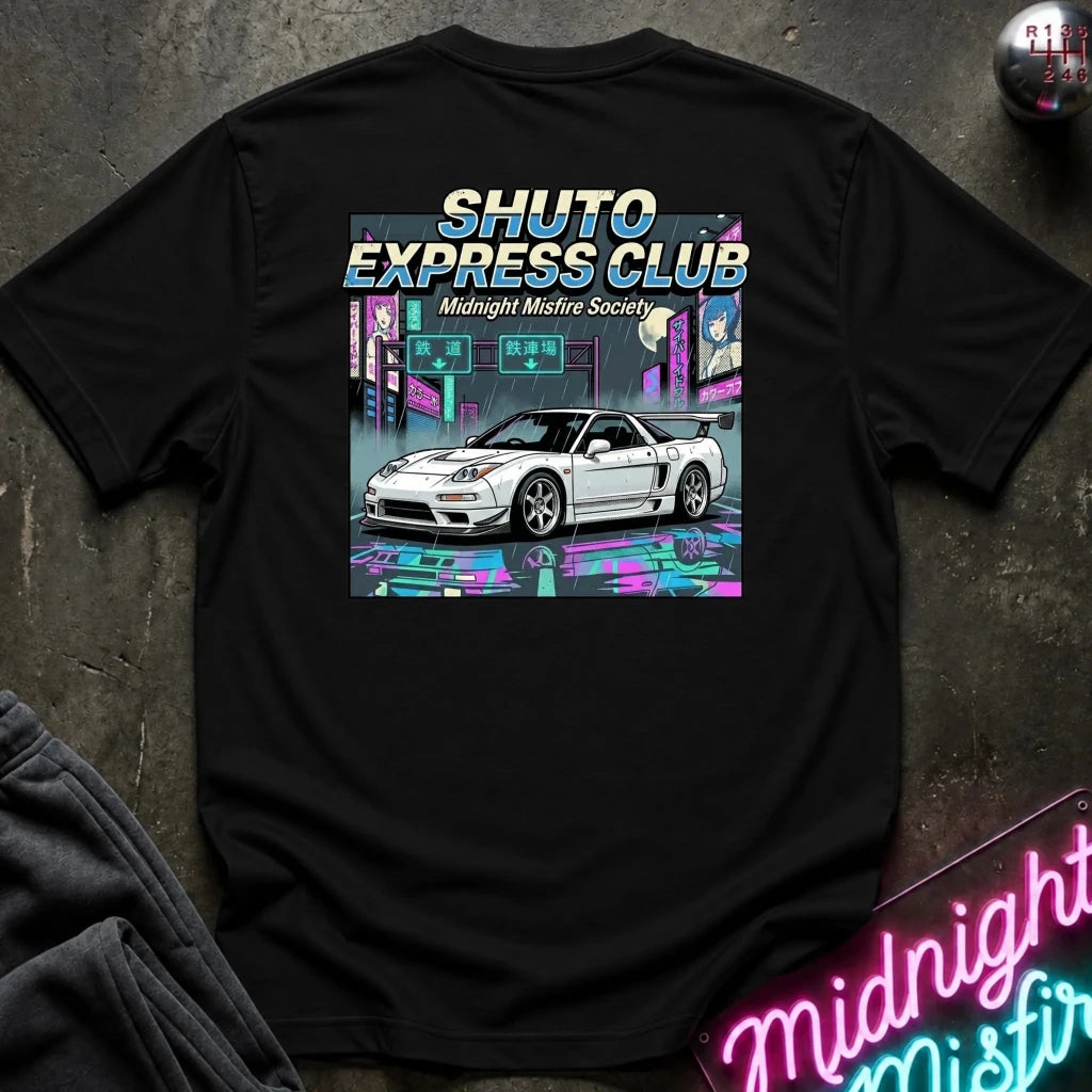 A black short-sleeve graphic T-shirt laid flat on a dark textured surface. The shirt features a large rectangular back print with the text 'SHUTO EXPRESS CLUB' and 'Midnight Misfire Society' above an illustration of a white sports car in a neon cyberpunk city scene.