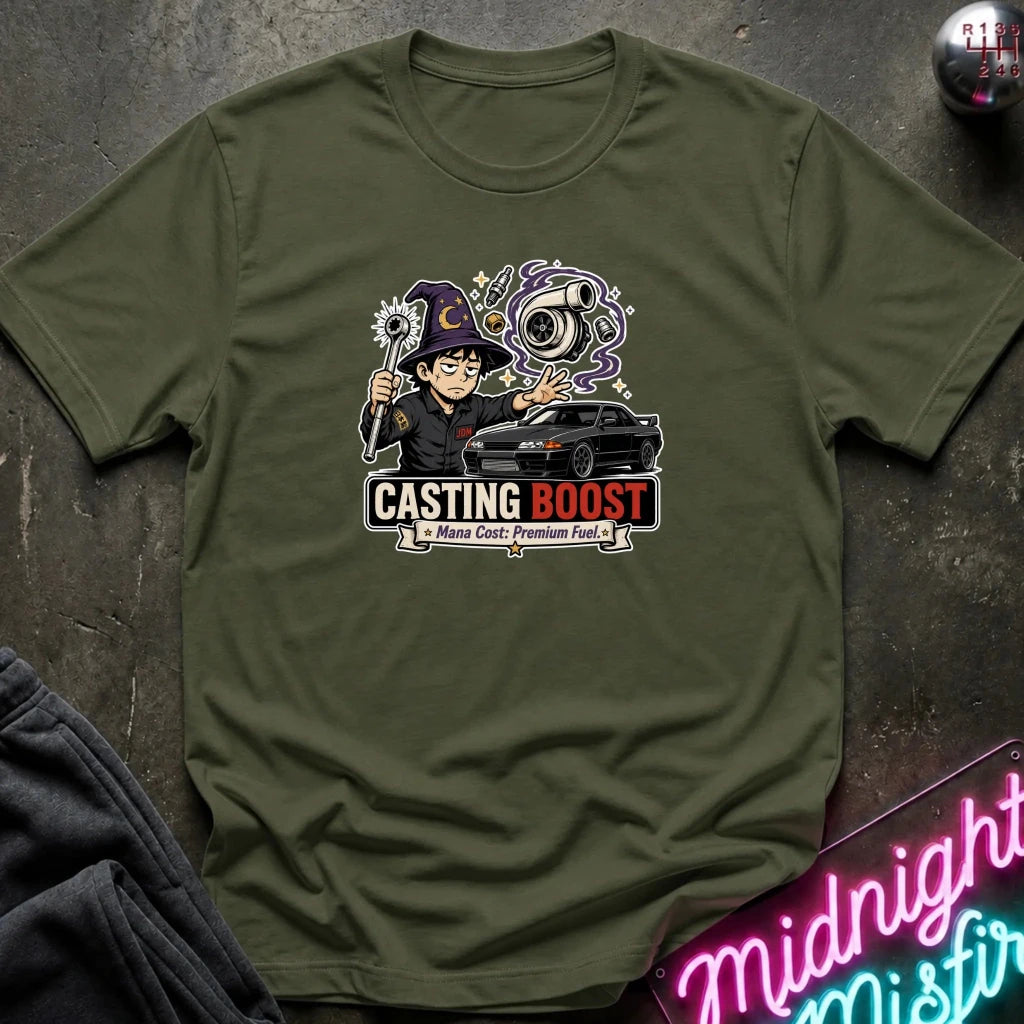An olive green crewneck t-shirt featuring a graphic print of a cartoon character with a witch hat and a black car, with the text 'CASTING BOOST' 