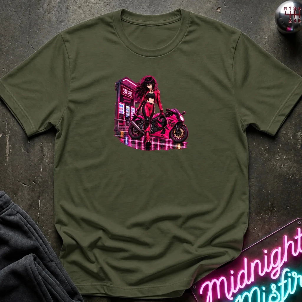 An olive green short-sleeve t-shirt laid flat on a dark textured surface, featuring a colorful graphic print of an anime-style woman in a red outfit standing next to a pink motorcycle in front of a neon sign. 