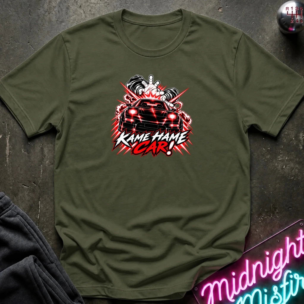 An olive green short-sleeve graphic t-shirt laid flat on a dark textured surface. The shirt features a red, white, and black graphic of a car with the text 'KAME HAME CAR!' in stylized lettering.