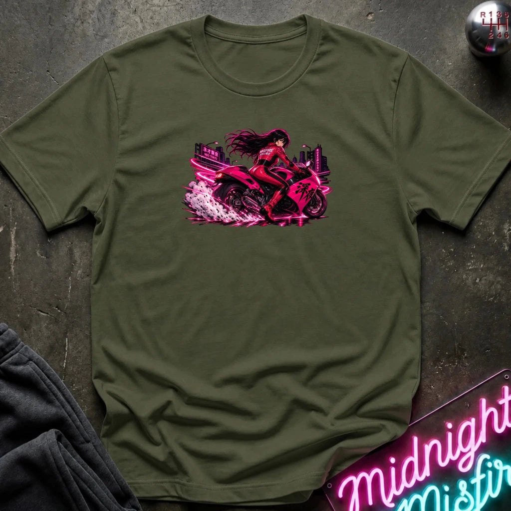 An olive green short-sleeve t-shirt laid flat on a dark textured surface, featuring a vibrant graphic of a woman riding a pink motorcycle with neon city lights.