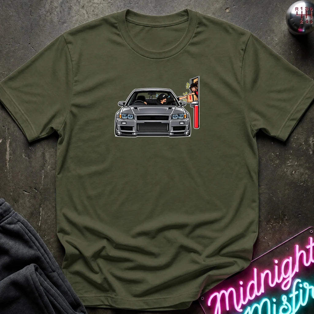 An olive green crewneck t-shirt laid flat on a dark textured surface, featuring a graphic print of a gray sports car and a vertical sign on the chest. 