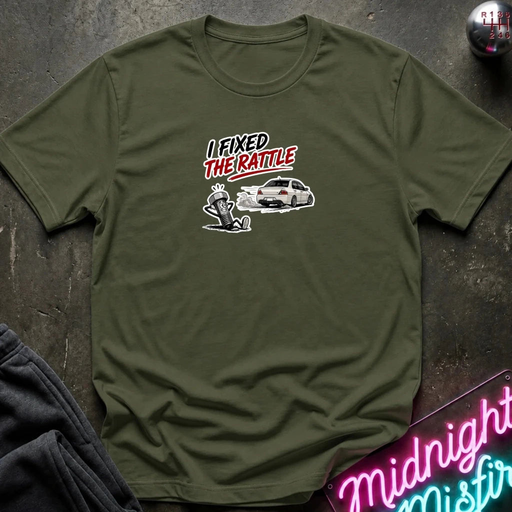 An olive green short-sleeve t-shirt with a graphic print on the chest reading 'I FIXED THE RATTLE' above a cartoon car 