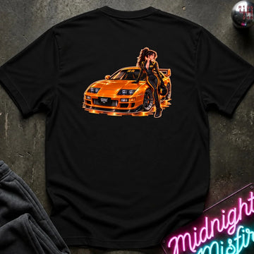 A black short-sleeve t-shirt laid flat on a dark textured surface, featuring a large graphic print of an orange sports car with a woman in a black outfit leaning on it. The shirt is styled with a gray sweatshirt, a gear shift knob, and a neon sign in the background.
