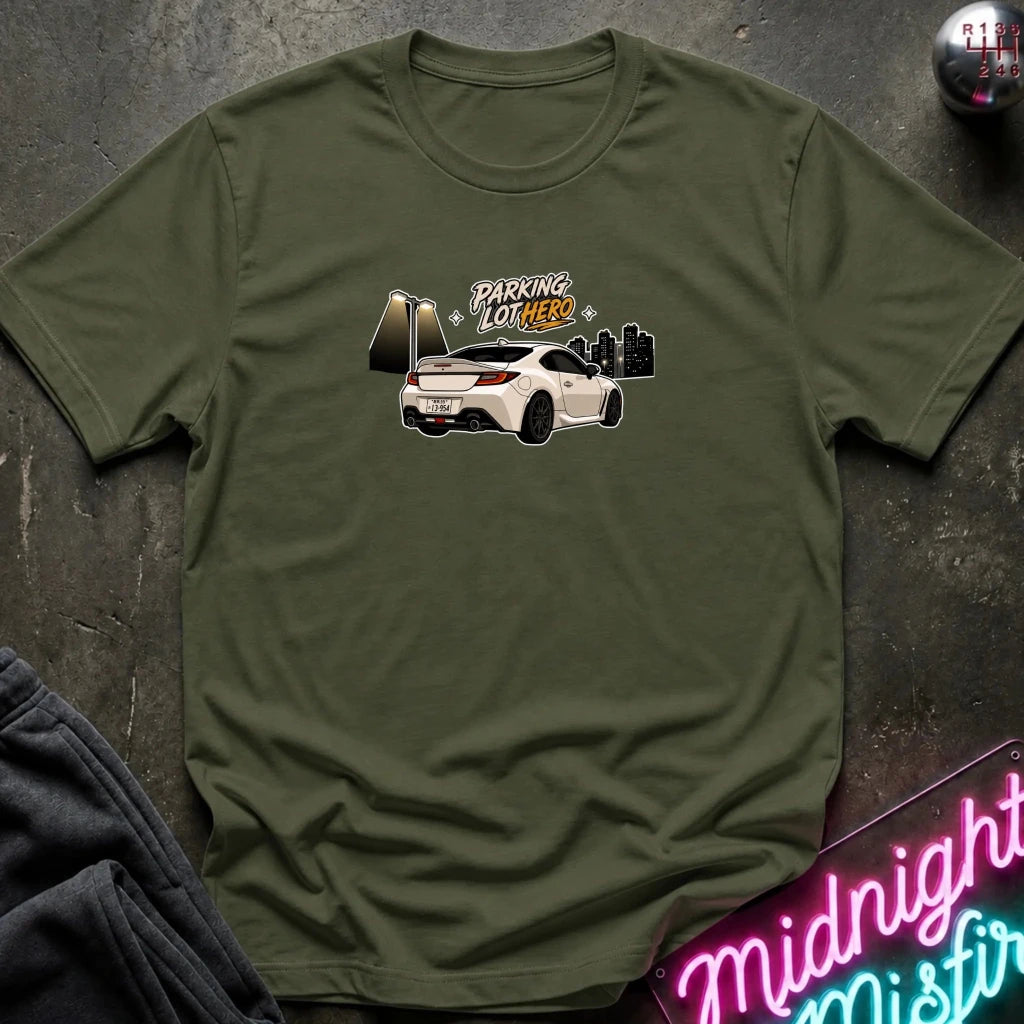 An olive green crewneck t-shirt laid flat on a dark textured surface, featuring a graphic of a white sports car with the text 'PARKING LOT HERO'