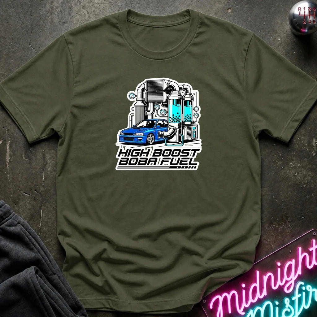 An olive green crewneck t-shirt featuring a graphic of a blue sports car with a high-performance engine and the text 'HIGH BOOST BOBA FUEL'. The shirt is displayed flat on a dark textured surface with a neon sign and dark pants partially visible.