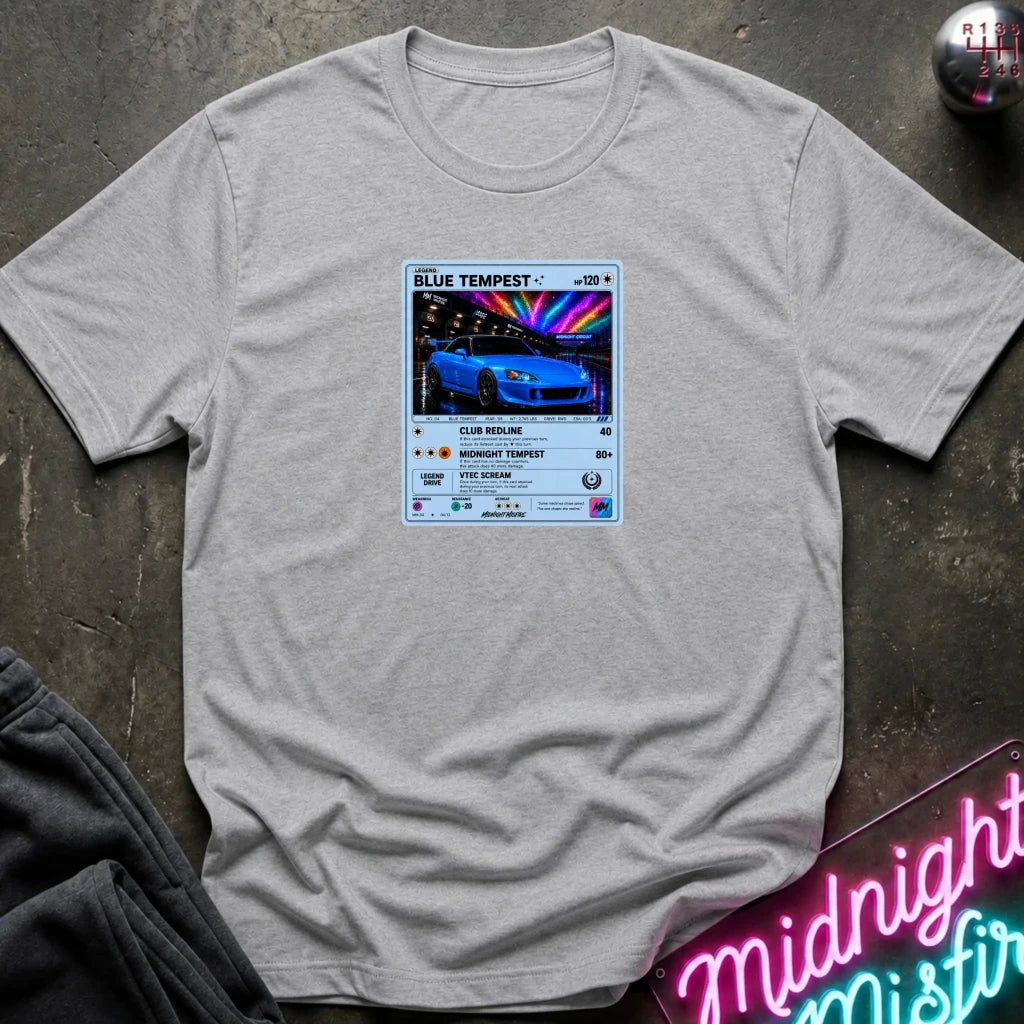 A light gray crewneck t-shirt laid flat on a dark textured surface, featuring a graphic print of vintage card and a car.