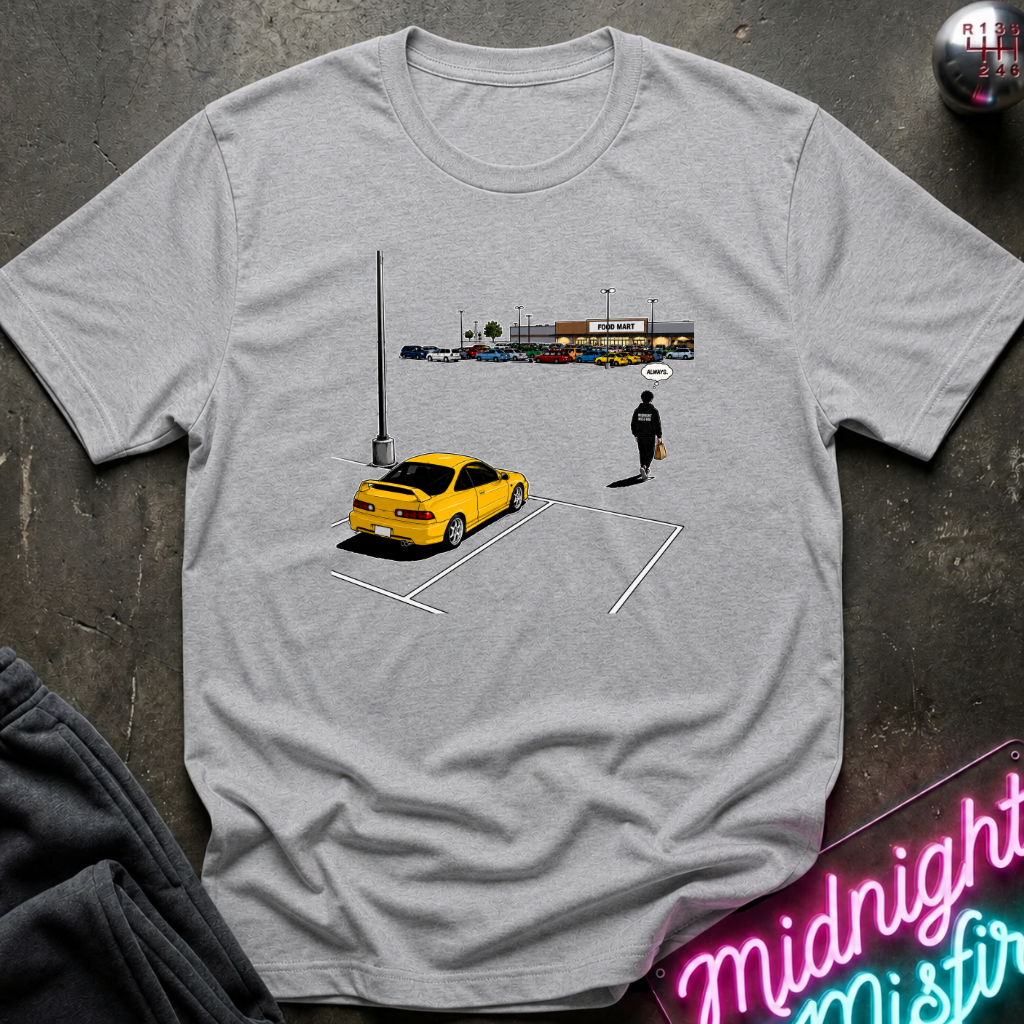 A light gray heather crewneck t-shirt featuring a graphic print of a yellow sports car in a parking spot next to a person, styled flat-lay on a dark textured surface with a neon sign and sweatpants.