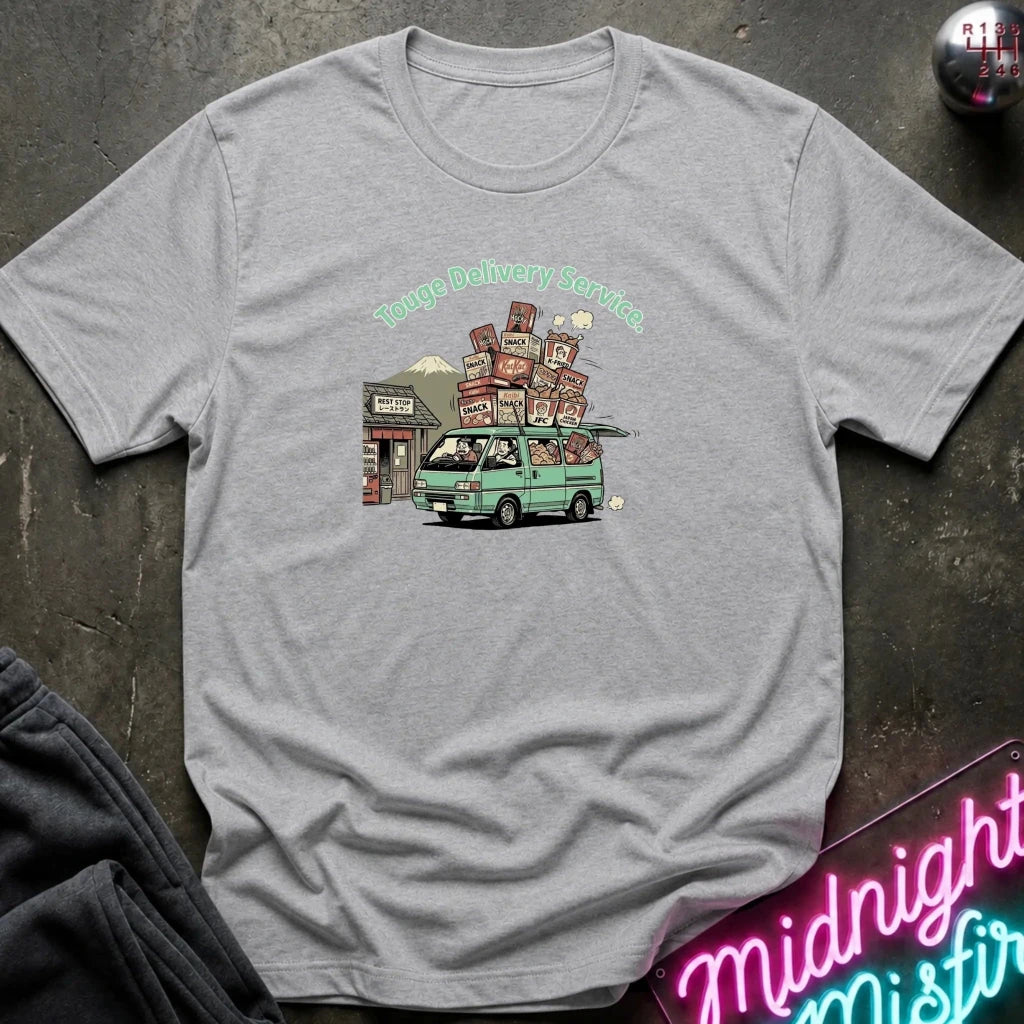 A heather gray short-sleeve t-shirt laid flat on a dark textured surface, featuring a colorful graphic of a green van carrying stacked boxes with the text 'Touge Delivery Service.' printed above it.