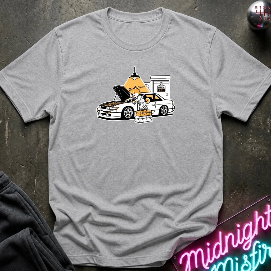 gray graphic t-shirt laid flat on a dark textured surface. The graphic features a dog fixing a car.