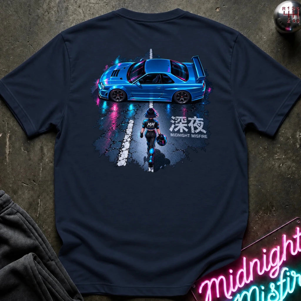 A navy blue t-shirt laid flat on a dark textured surface, featuring a large graphic print on the back of a blue sports car on a wet road with a motorcycle rider and Japanese text. 