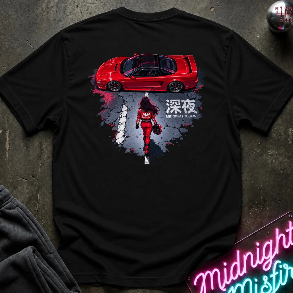 A black short-sleeve graphic T-shirt laid flat on a dark textured surface. The shirt features a large back print showing a red sports car above a red racer in a splattered gray and black design