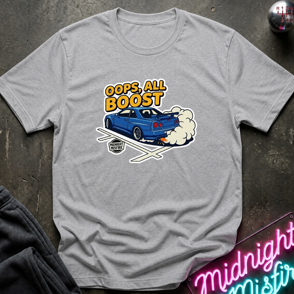 A heather gray crewneck t-shirt featuring a graphic of a blue sports car doing a burnout with the text 'OOPS, ALL BOOST' in yellow. The shirt is laid flat on a dark textured surface with a neon sign and dark pants partially visible.