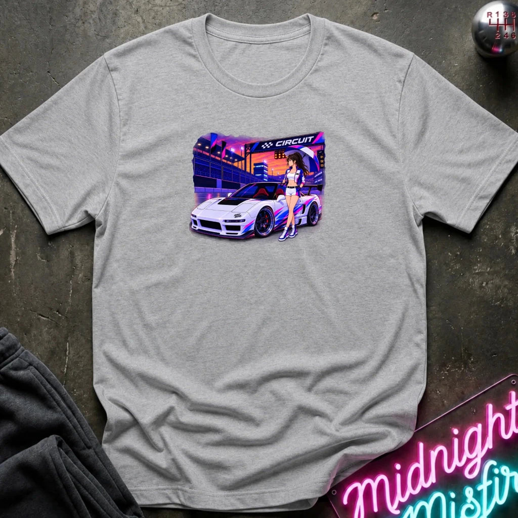 A light heather gray short-sleeve t-shirt laid flat on a dark textured surface, featuring a colorful graphic print of a white sports car and a woman in a neon-lit scene. 