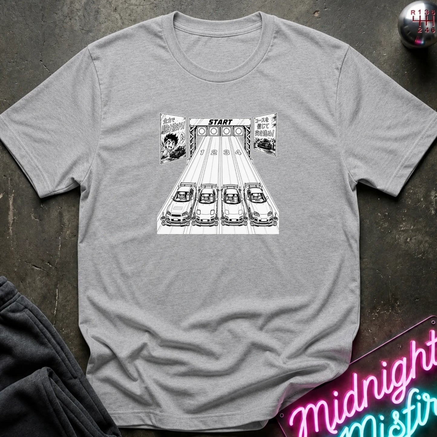 A light gray  short-sleeve t-shirt laid flat on a dark textured surface, featuring a black-and-white graphic of 4 cars lined up at a racing on a track.