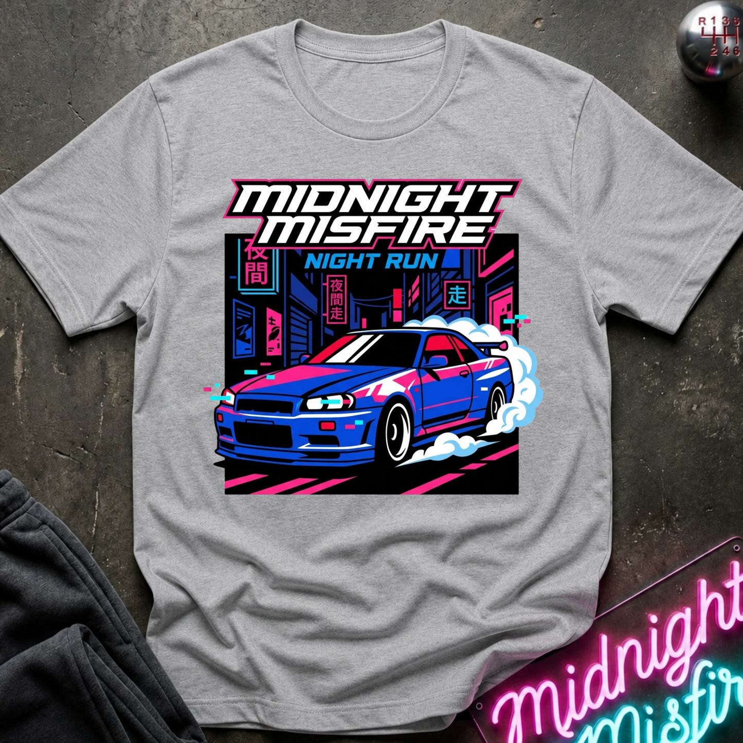 A light gray crewneck t-shirt featuring a vibrant graphic print of a blue sports car drifting in front of neon-lit city buildings. The text 'MIDNIGHT MISFIRE' is printed above the car in a stylized white and pink font, with 'NIGHT RUN' below it.
