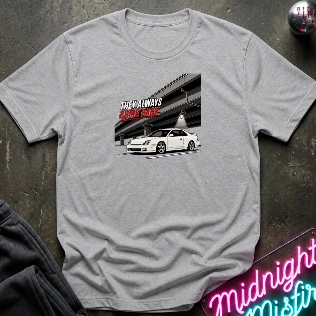 A light gray heather crewneck t-shirt laid flat on a dark textured surface. The shirt features a graphic print of a white sports car under an overpass 
