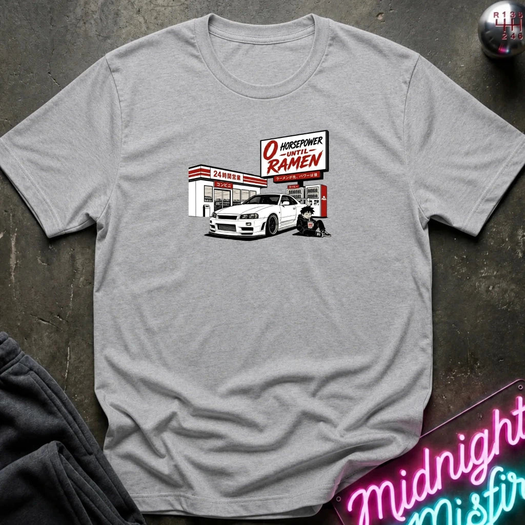 A heather gray crewneck t-shirt laid flat on a dark textured surface, featuring a graphic print of a white sports car parked in front of a konbini.