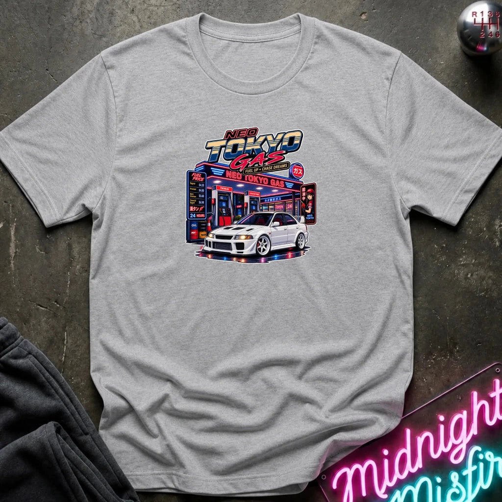 A heather gray short-sleeve crewneck t-shirt featuring a 'Neo Tokyo Gas' graphic with a white sports car, laid flat on a dark textured surface with a neon sign and sweatpants as props.