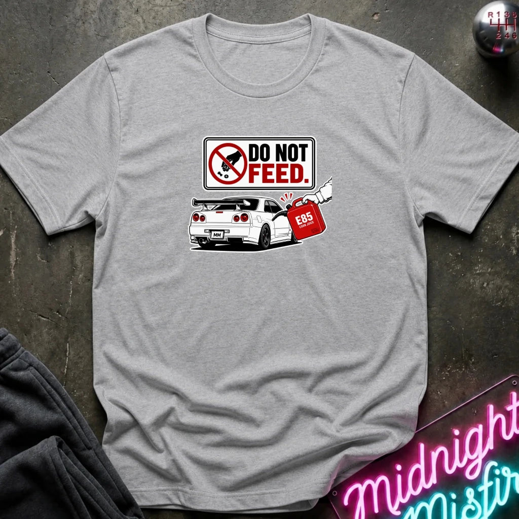 A grey short-sleeve graphic t-shirt laid flat on a dark textured surface. The graphic features a 'DO NOT FEED' sign.