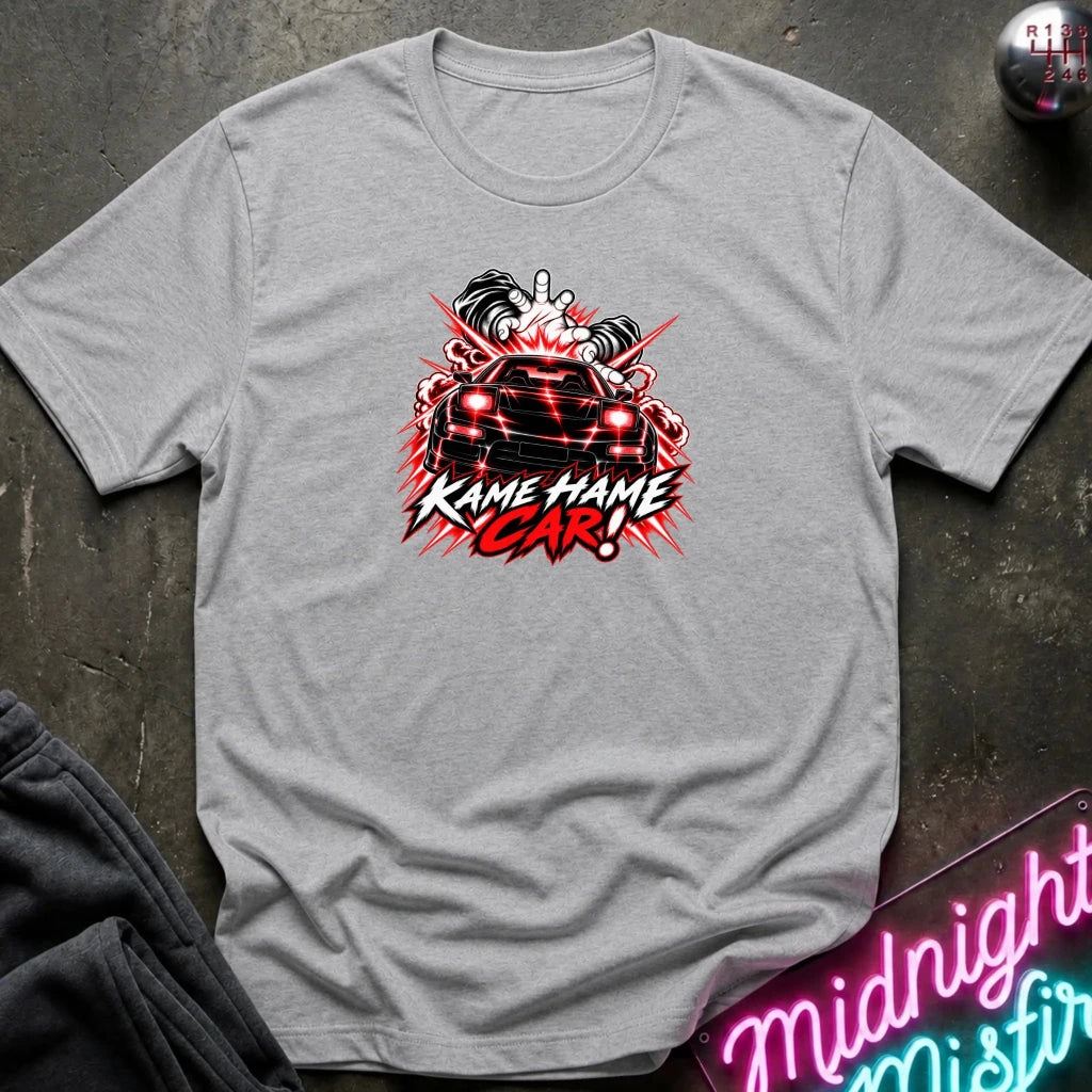 A heather gray short-sleeve graphic t-shirt laid flat on a dark textured surface. The shirt features a red, white, and black graphic of a car with the text 'KAME HAME CAR!' in stylized lettering.