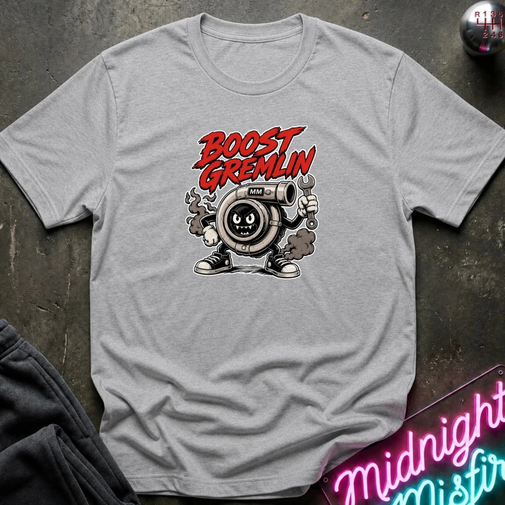 A light gray crewneck t-shirt featuring a cartoon graphic of a turbocharger character with the text 'BOOST GREMLIN' in red, laid flat on a dark textured surface.
