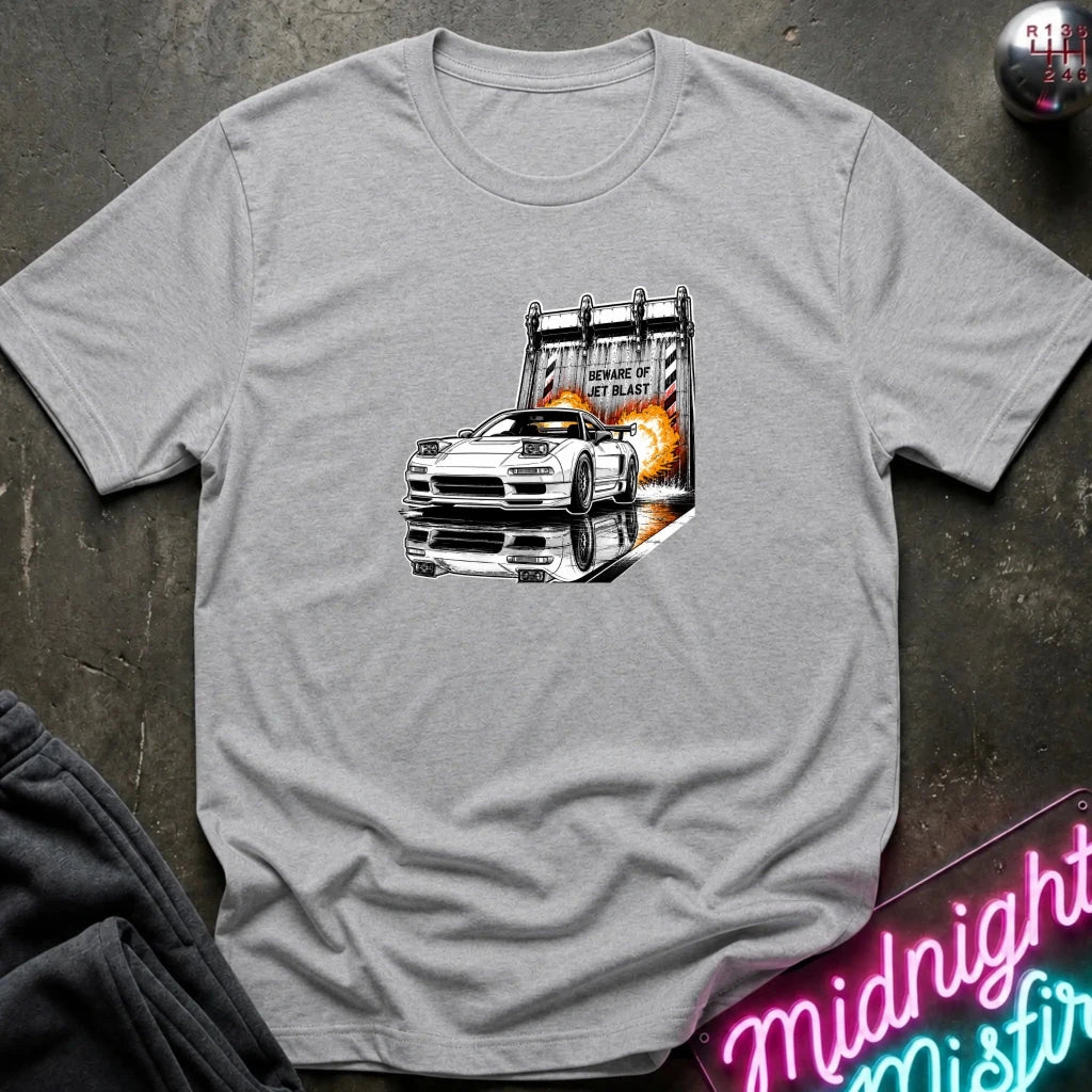 A light gray heather  short-sleeve t-shirt laid flat on a dark textured surface, featuring a graphic print of a white sports car in front of a blast off area.