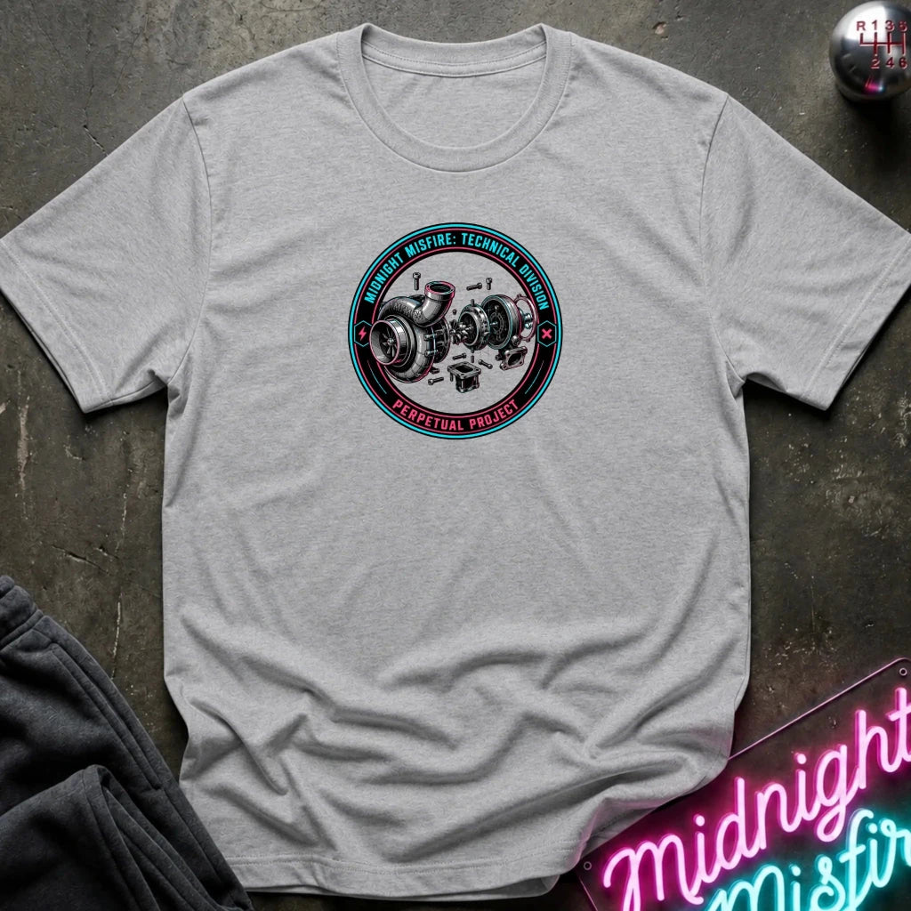 A light gray crewneck t-shirt laid flat on a dark textured surface, featuring a circular graphic on the chest with a turbocharger illustration and the text