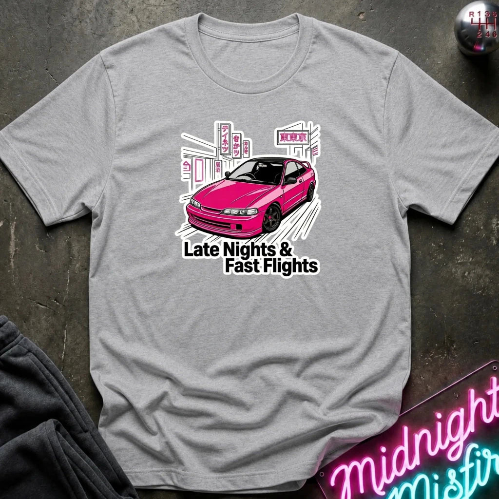 A heather gray crewneck t-shirt laid flat on a dark textured surface. The shirt features a graphic of a pink car with white and black text reading 'Late Nights & Fast Flights'.