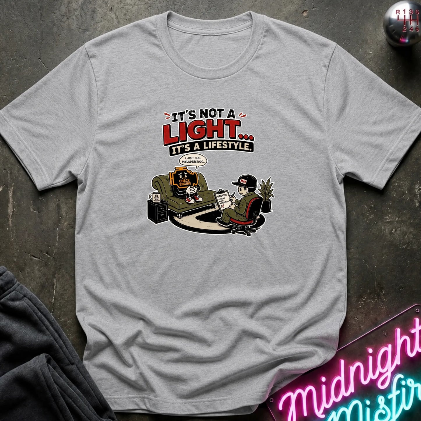 A light gray heather crewneck t-shirt featuring a cartoon graphic of two characters sitting in a room, with the text 'IT'S NOT A LIGHT.