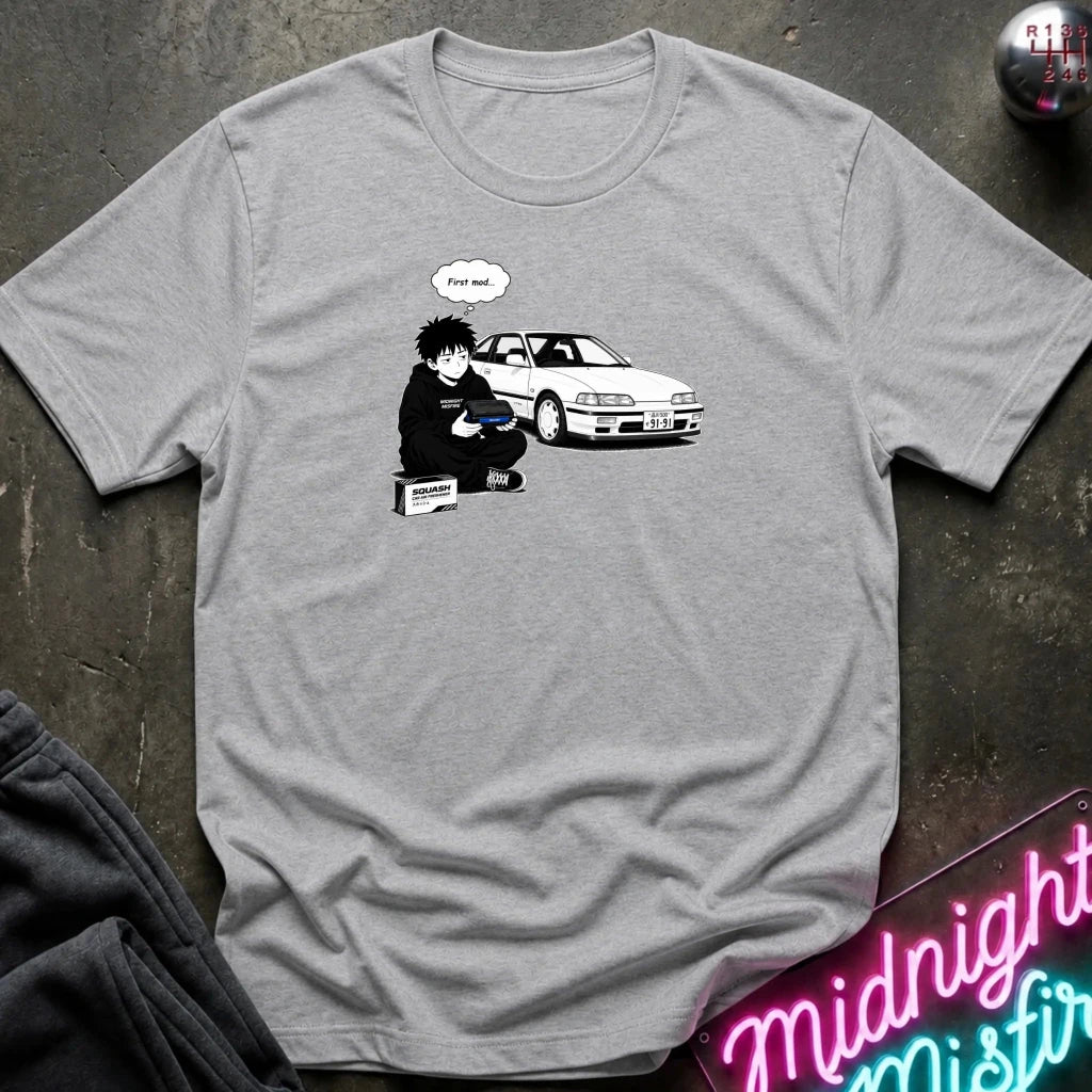 A heather gray crewneck t-shirt featuring a graphic print of a cartoon character sitting next to a white sports car with a speech bubble 