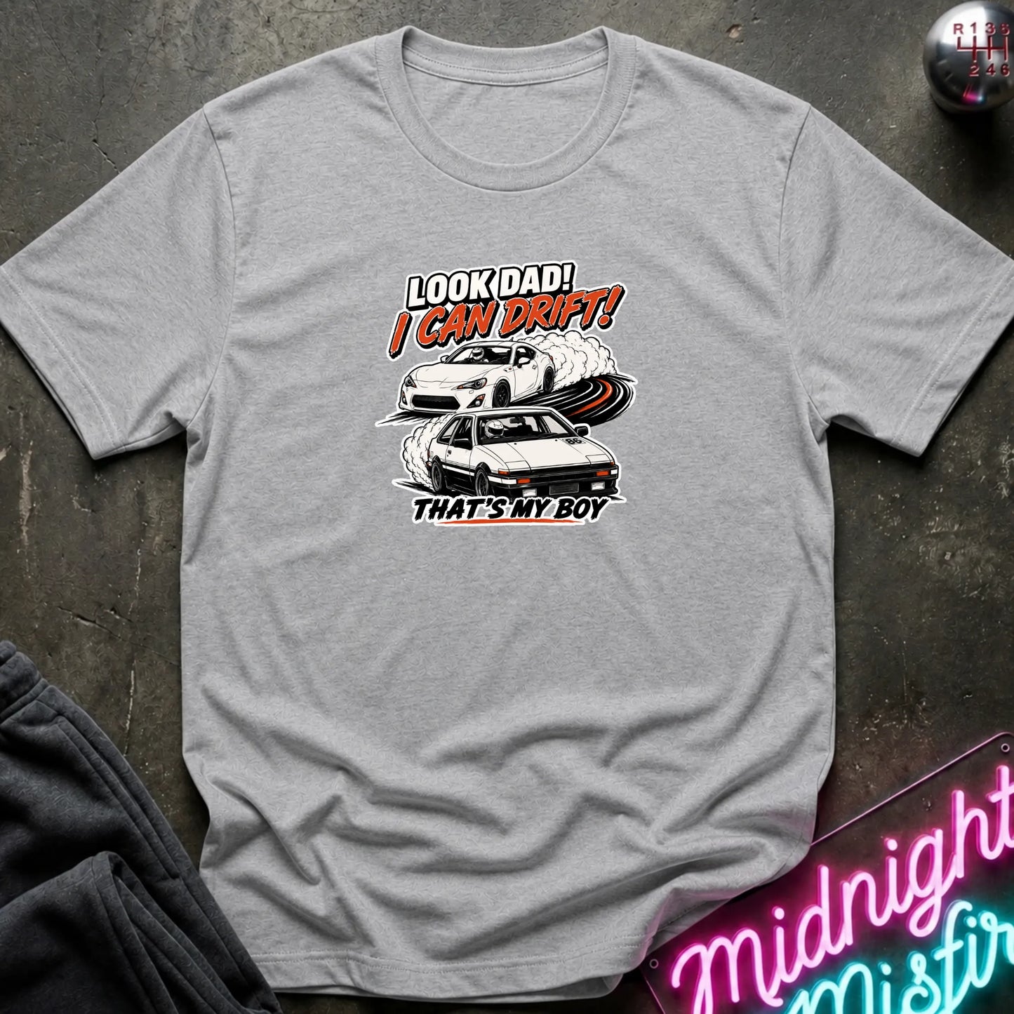 A heather gray  short-sleeved t-shirt  that has a cars drifting which are older and newer generations of toyotas.