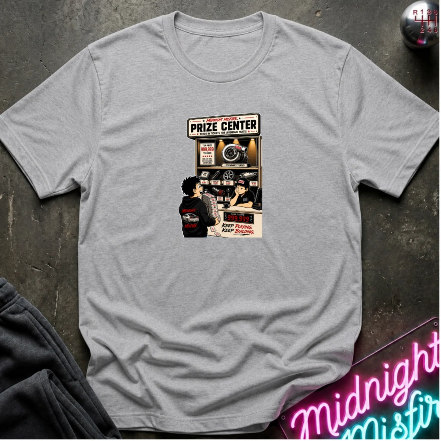 a heather gray short-sleeve crewneck t-shirt laid flat on a dark textured surface, featuring a central graphic print of a prize center for car parts. 