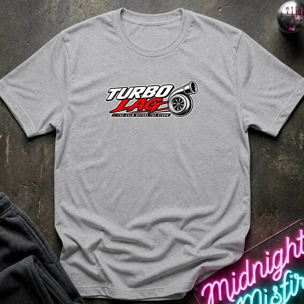 A heather gray short-sleeve t-shirt laid flat on a dark textured surface, featuring a 'Turbo Lag' car logo graphic in red, white, and black on the chest.
