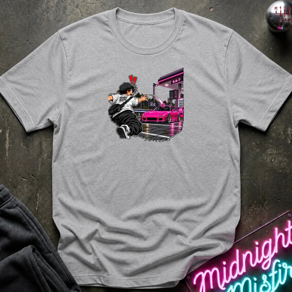 A light gray heather short-sleeve crewneck t-shirt laid flat on a dark textured surface. The center of the shirt features a graphic print of an anime character in a black and white outfit with a hat, next to a sports car 