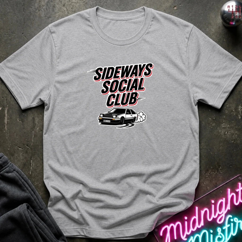 A heather gray short-sleeve t-shirt with a graphic print that reads 'SIDEWAYS SOCIAL CLUB' above a black car with white smoke, laid flat on a dark textured surface with partial props visible at the edges.