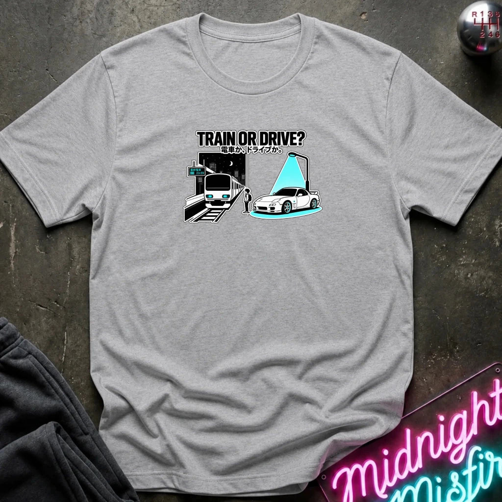 gray graphic t-shirt laid flat on a dark textured surface. The graphic features a train and a car with a person.