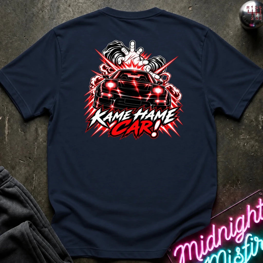 A navy blue t-shirt laid flat on a dark textured surface, showing a large back graphic of a black car with red lights, smoke, and the text 'KAME HAME CAR!' in red and white. 